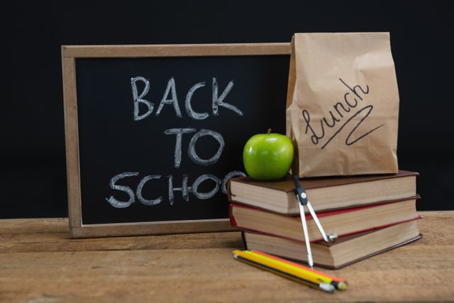 Lunch paper bag, green apple and slate with text back to school on wooden table against black background