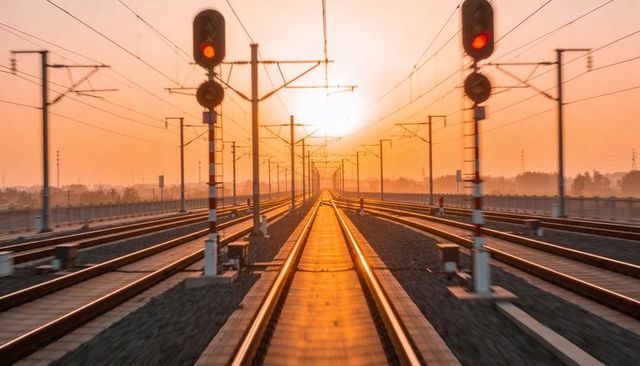 Golden hour railway tracks on elevated viaduct with red signals and overhead catenary