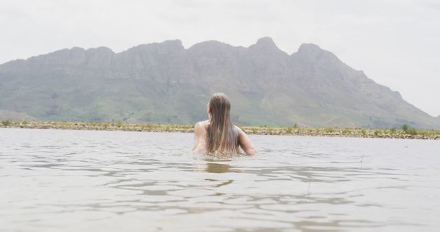 Tranquil scene of a woman swimming in a lake with a majestic mountain range in the background. Suitable for travel websites, outdoor and adventure promotions, wellness articles, and nature appreciation content.