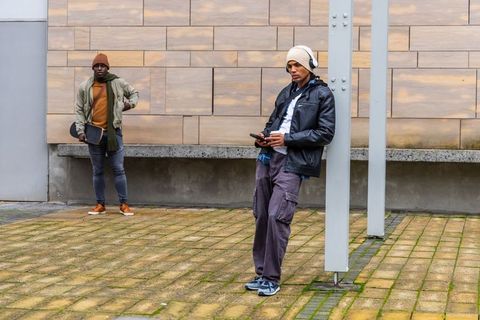 Young men leaning at urban plaza holding phone and headphones wearing streetwear