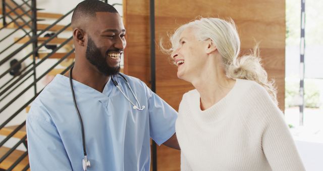 Healthcare worker in blue scrubs interacting joyfully with elderly female patient, creating a warm and friendly atmosphere. Image can be used for promotional materials related to caregiving services, senior healthcare, medical facilities, or any content focused on positive patient experiences.