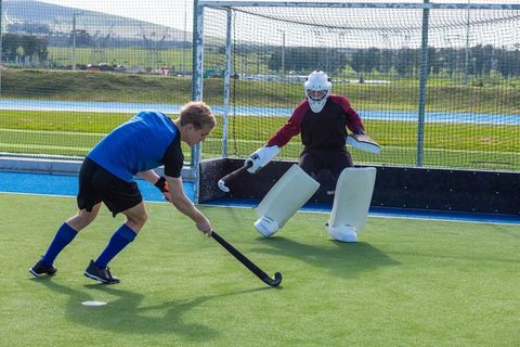 Field hockey player facing determined goalkeeper