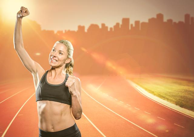 Woman wearing sports attire raising hand in victory on an empty running track with city skyline in the background. Useful for fitness promotions, sports-related advertising, motivational content, and health and wellness campaigns.
