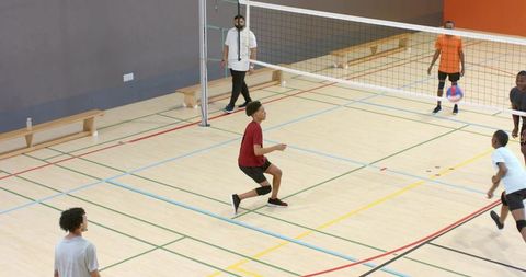Diverse male volleyball players playing indoor gym court preparing to receive serve