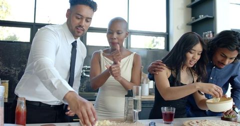 Multicultural friends preparing homemade pizza on modern kitchen island at casual party