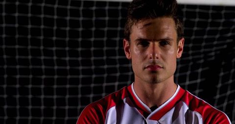 Confident soccer player posing in red white jersey against goal net