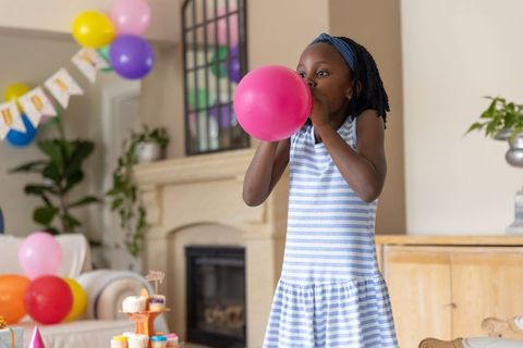Girl inflating pink balloon at home birthday party with cupcakes and colorful decor