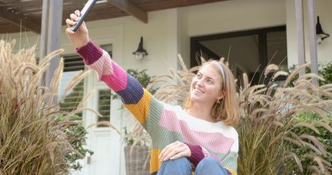 Woman Taking Selfie on Front Porch with Stylish Sweater and Nature Backdrop