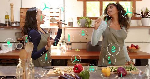 Women singing and cooking with wooden spoons in bright kitchen surrounded by eco icons