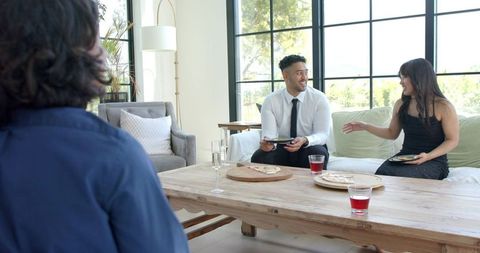 Diverse friends enjoying pizza and drinks in modern bright living room with large windows