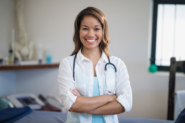 This image depicts a confident female therapist standing with arms crossed in a hospital ward, smiling warmly. Ideal for use in healthcare-related content, medical websites, hospital brochures, and promotional materials for medical services.