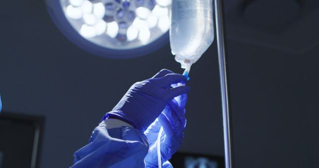 Gloved hands of a medical professional are seen preparing an IV drip in a hospital environment, likely in an operating room. This image is ideal for healthcare and medical-related content, illustrating the preparation process, healthcare services, surgical procedures, and the experience of medical staff.