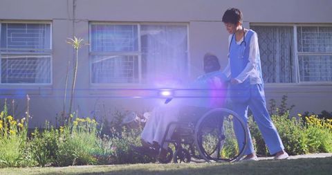 Caring Nurse Pushing Happy Senior Man in Wheelchair Outside