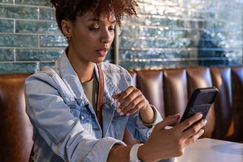 African american woman using smartphone in cafe booth wearing denim jacket urban lifestyle