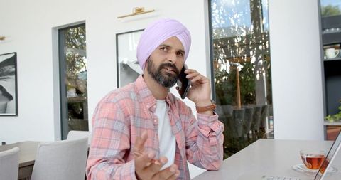 Man with Turban Working from Home on Phone and Laptop at Desk