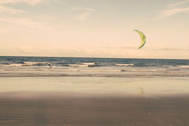 Solo kite surfer enjoying waves on an isolated sandy beach. Ideal for images promoting beach activities, adventure sports, and serene coastal landscapes.