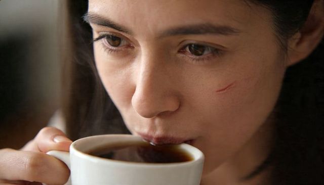 Woman sipping coffee in cozy nook showing light cheek scratch, closeup portrait