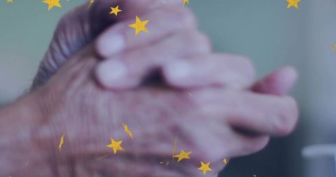 Clasping senior hands revealing wrinkles, veins and age spots with golden star overlay