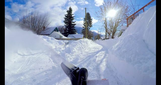 Snowblowing suburban street during winter with houses and trees in background and bright blue sky. Ideal for content related to winter activities, suburban life, cold weather conditions, and snow removal