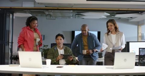 Diverse team collaborating around tablet with laptops and printed charts in modern office