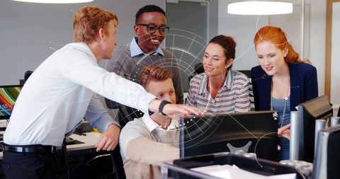 Professionals collaborating around computer monitor, pointing at screen in bright office