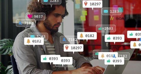 Bearded man typing at laptop in coworking space surrounded by social media notification icons