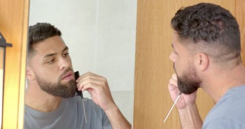 Man grooming beard using multi-tool comb-razor in bathroom