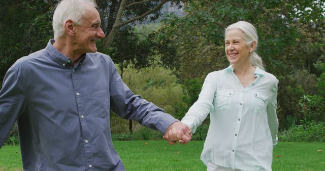 Front view of a happy senior Caucasian man and woman holding hands and walking in a garden