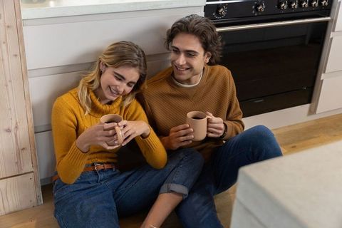 Happy Couple Relaxing on Kitchen Floor with Coffee Mugs
