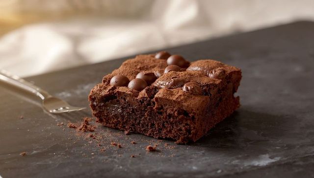 Showcasing fudgy chocolate brownie with glossy chocolate pearls and cocoa dusting on slate