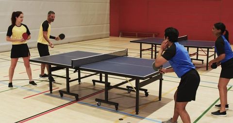 Diverse Teams Engaged in Competitive Table Tennis Doubles in Gym