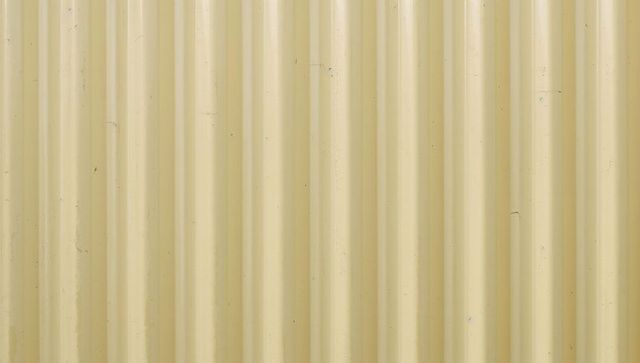 Beige corrugated metal siding with weathered vertical ribs and paint scuffs