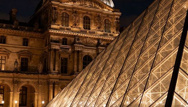 Nighttime louvre pyramid glass prism illuminated reflecting on historic museum facade