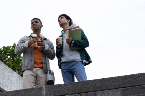 Two student friends standing on campus ledge holding coffee and notebooks during break