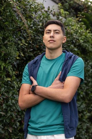 Young man standing confidently in backyard wearing teal tee and navy zip-up hoodie