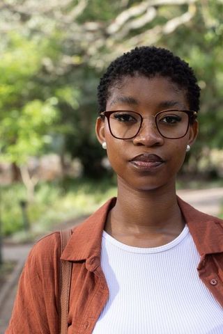 Confident african woman wearing round glasses and rust shirt standing on park path