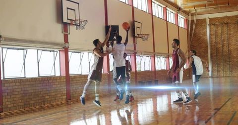 High school basketball player jumping for layup while defender contesting shot in gym