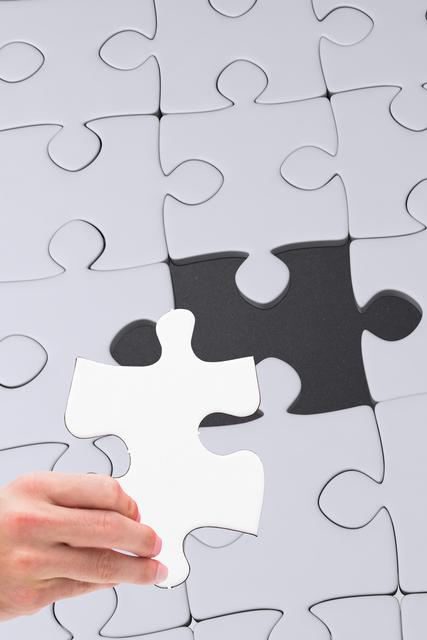 Hand holding puzzle piece and placing it into final open spot, representing solving problems, achieving goals, and finding solutions. Perfect for concepts related to teamwork, problem-solving, strategy, and success. Useful for presentations, educational materials, blogs, and advertisements emphasizing collaboration and strategic thinking.