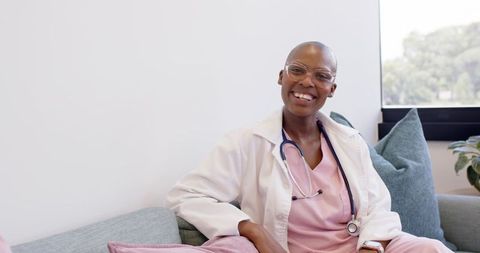 Smiling clinician relaxing on couch in clinic lounge with stethoscope and pink scrubs