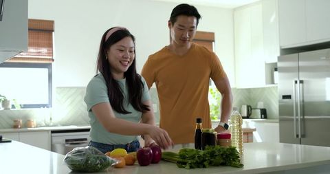 Asian couple preparing healthy meal at modern kitchen island with fresh produce and herbs