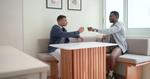 Diverse male friends toasting with green drinks at modern built-in banquette in apartment