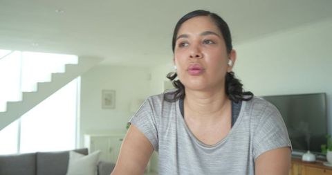 Woman cycling on stationary bike wearing wireless earbuds in minimalist living room