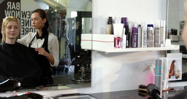 A Caucasian hairstylist is working on a female client's hair in a salon, surrounded by various hair products and tools, with copy space. Their focused expressions and the salon environment suggest a professional hairdressing session in progress.
