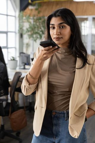 Indian woman speaking into smartphone in modern open-plan office wearing blazer