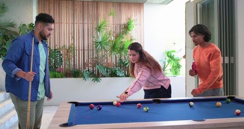 Diverse friends playing pool on sunny patio with blue-felt table, cues and drinks