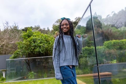 Smiling african american girl standing by glass balustrade in lush backyard wearing sweater