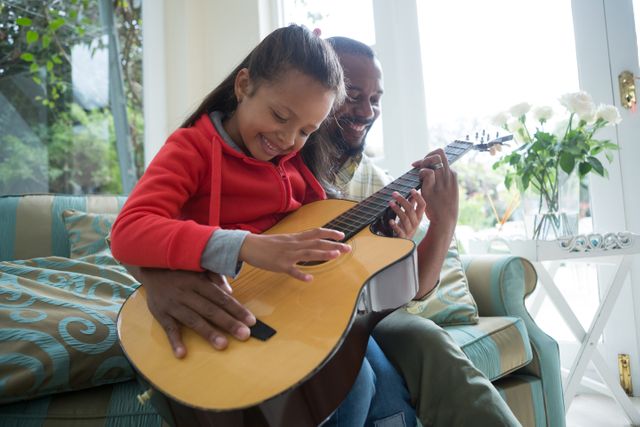 Father and daughter enjoying quality time playing guitar together in a cozy living room. Perfect for illustrating family bonding, music education, parenting, and joyful moments at home. Ideal for use in advertisements, educational materials, and family-oriented content.