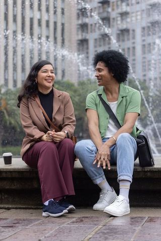Multicultural couple sitting by city fountain sharing laughter and coffee