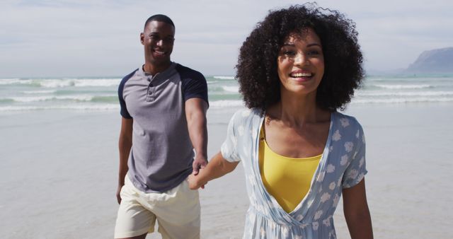 Smiling african american couple walking and holding hands at the beach. healthy outdoor leisure time by the sea.