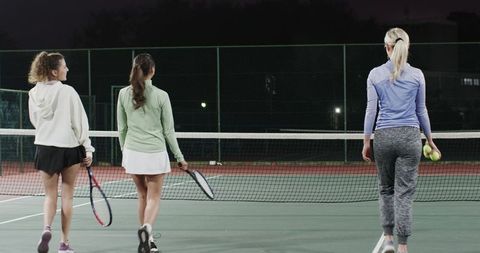 Women walking toward tennis net on lit outdoor court at night